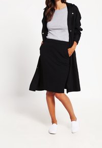 Musta pitkä takki harmaan paidan päällä, yhdistetty mustaan hameeseen ja valkoisiin kenkiin. Puuvillasekoitekangasta, slim fit -design ja minimaalinen varustus.