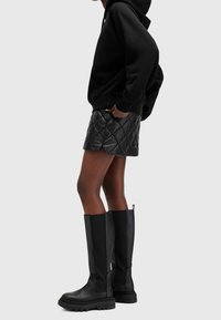 Black quilted leather skirt with side split, paired with a black hoodie and knee-high black boots with back pull tabs.