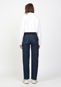 Dunkelblaue gerade geschnittene Jeans werden mit einem verkürzten weißen Shirt getragen. Die Jeans verfügen über ein klassisches Fünf-Taschen-Design und dezente Nähte.