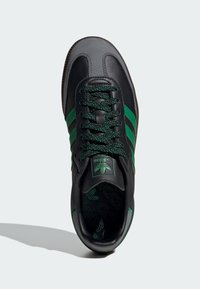 Black leather sneaker featuring green stripes, textured laces, and a padded tongue with an embossed logo on a patterned insole.
