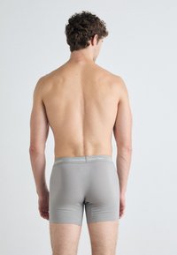 Grå boxershorts med en myk elastisk midjebånd med "Calvin Klein"-logo. Stoffet har en glatt tekstur og en tettsittende design.