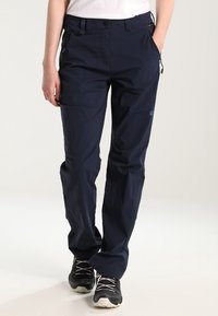 Person wearing navy blue outdoor pants and black hiking shoes, standing with hands in pockets on a white background.