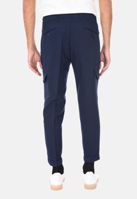 Pantaloni cargo navy con una vestibilità affusolata, realizzati in un tessuto morbido. Presentano due tasche laterali, due tasche posteriori e polsini alle caviglie. Indossati con scarpe da ginnastica bianche.
