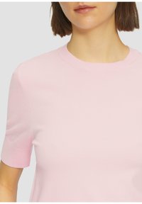 Lichtroze gebreid T-shirt met korte mouwen en een ronde hals, gladde textuur en een getailleerd ontwerp. Naaddetails op de mouwen.