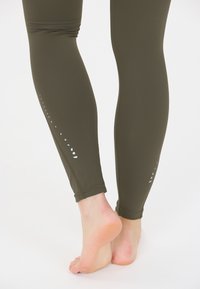 Olivgröna träningsleggings med en åtsittande design, prydda med reflekterande prickar längs sidan och sömlösa nederkanter. Slen yta.