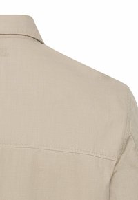 Dos de chemise en tissu beige avec col et coutures visibles le long de l'épaule et de la partie supérieure du dos.