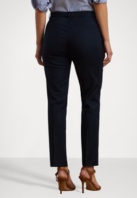 Námořnické kalhoty na míru s hladkou texturou a slim fit. Mají zadní kapsy a středně vysoký pas, doplněné hnědými sandály na vysokém podpatku.