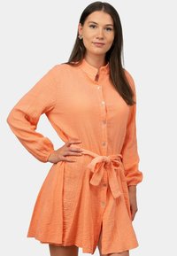 Abito camicia lungo color pesca con maniche lunghe in tessuto testurizzato, con chiusura a bottoni, colletto e cintura regolabile in vita.