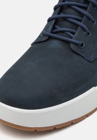 Pantofii din suede bleumarin au o textură netedă, vârf rotund și talpă din cauciuc alb contrastant, cu un model texturat și accente din cauciuc natural.