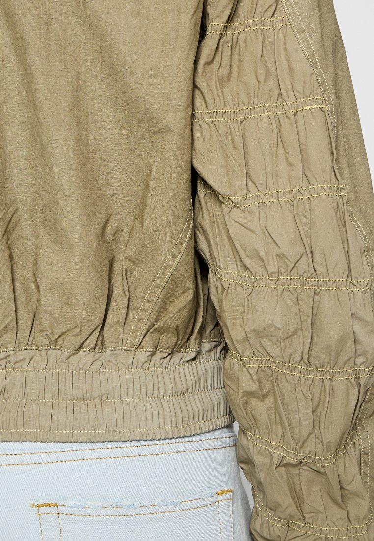 Olivgrüne Bomberjacke mit strukturierten, gerafften Ärmeln und elastischen Bündchen. Verfügt über sichtbare Nähte und einen gerippten Taillenbund. Lässiges Design.