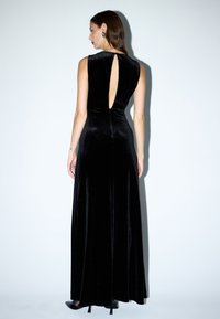 Zwart fluwelen maxi-jurk met een hoge hals en een keyhole achterkant, voorzien van een aansluitend lijfje en een vloeiende rok; enkel-lang met een gladde structuur.