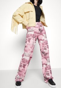 Pantalons roses à motifs avec des graphiques, associés à une veste jaune à franges. Le tissu semble doux, et le design inclut diverses textures.