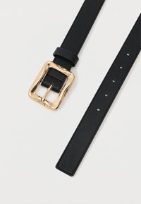 Čierny kožený opasok s lesklou, mierne vlnitou zlatou štvormilou s príchytkami na viacero nastavení na bielom pozadí.