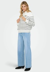 Białe i granatowe paskowane bluza z kapturem z kieszenią kangurką, zestawiona z jasnoniebieskimi szerokimi spodniami dżinsowymi i czarnymi botkami na obcasie.