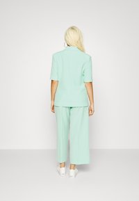 Mintgroene blazer en brede pantalon van een zachte stof, gecombineerd met witte sneakers. De blazer heeft korte mouwen en een kraag.