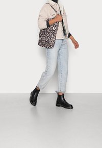 Kraftiga svarta ankelstövlar, ljusblå tapered jeans, beige kordjacka med fleecekrage och en axelväska i leopardmönster.