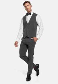 Costume trois pièces gris avec gilet, chemise blanche et nœud papillon noir. Tissu texturé, design ajusté et chaussures en cuir noires.
