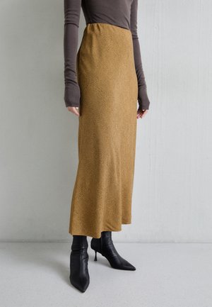 Brązowa bluzka z długim rękawem w połączeniu z wysokim, musztardowym żakietem z teksturowanym wzorem, uzupełnione czarnymi, spiczastymi botkami za kostkę.