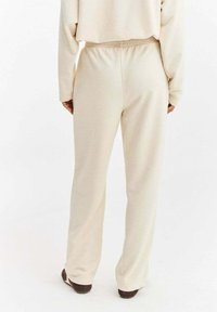 Béžové kalhoty s elastickým pasem a rovnými nohavicemi, vyrobené z měkké látky s hladkou texturou bez viditelných vzorů nebo zdobení.
