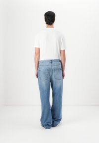 Jeans de mezclilla azul claro con un ajuste relajado y cinco bolsillos, combinados con una camiseta blanca de manga corta sencilla, vistos desde atrás.