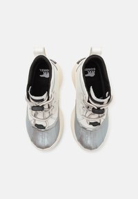 Zapatillas con un diseño blanco y plateado, que cuentan con una parte superior texturizada en plateado, interior negro y cordones elásticos con cierres de tipo toggle.