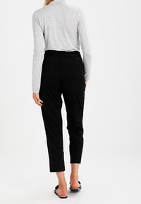 Černé kalhoty s vysokým pasem a zúženým střihem. Vyrobené z hladké látky, s opaskem na zadní straně a minimálními detaily švů.