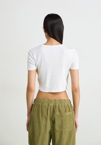 T-shirt bianco cropped con maniche corte, tessuto testurizzato, abbinato a pantaloni in velluto a coste verdi oliva con tasca posteriore e vita elastica.