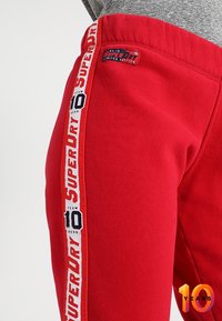 Rode sweatpants met een gestructureerde afwerking, voorzien van een zijpaneel met "SUPERDRY" in het wit gedrukt en een limited edition label op de tailleband.