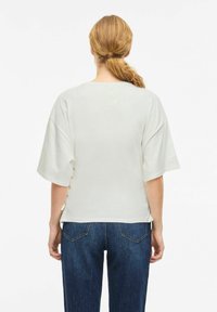 Hvit kortermet skjorte med løs passform og sidelommer med knappedetaljer, kombinert med mørkeblå jeans. Materiale i bomullsblanding, avslappet design.