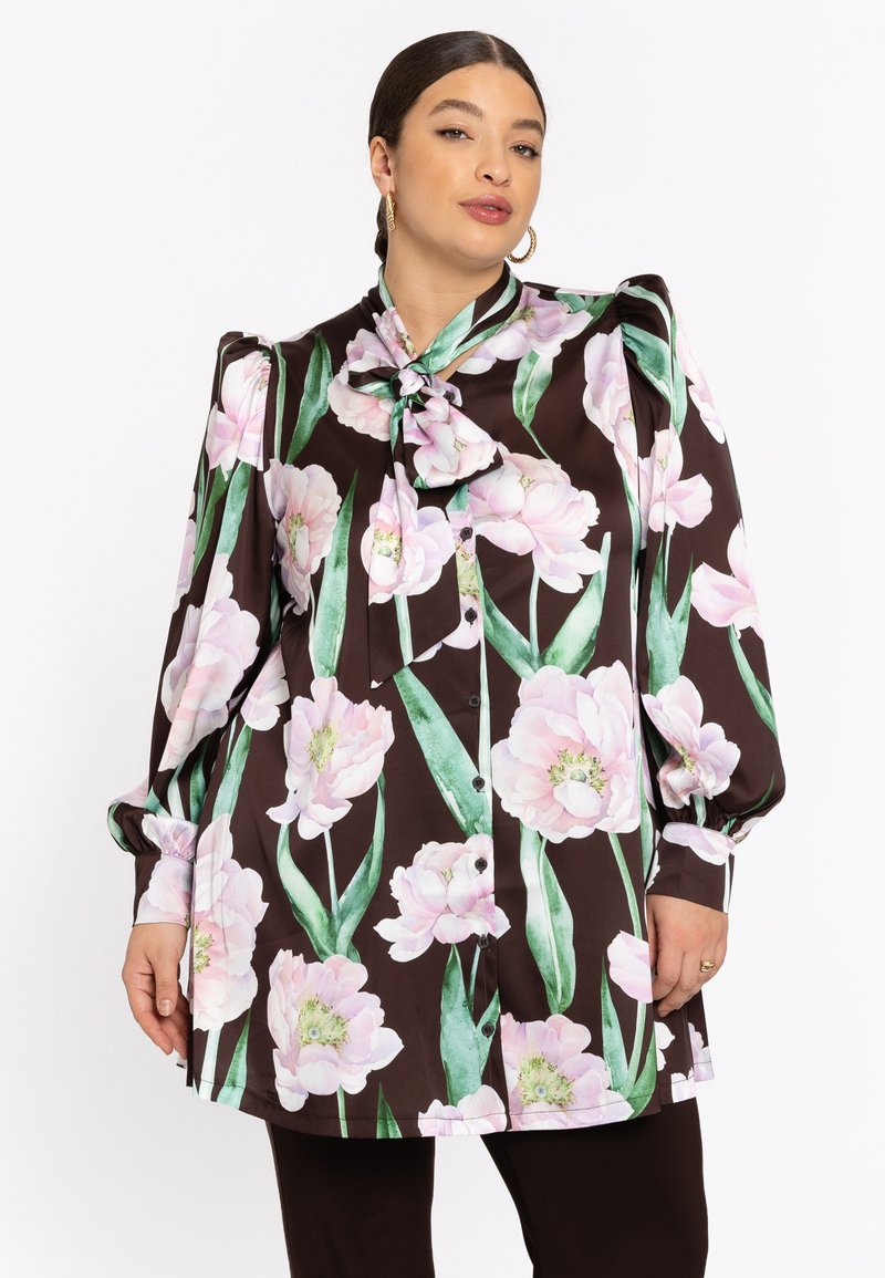 Braune Bluse mit großem rosa Blumenmuster, Schleifenkragen, Knopfverschluss, lange Ärmel mit gerafften Manschetten, glatte Stofftextur.