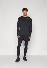 Svart langermet treningsskjorte med delvis glidelås, sammen med svarte shorts og tights. Svart sneakers, glatt tekstur, minimal merkevaredetalj.