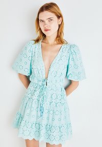 Robe bleu clair, longueur genou, en tissu à trous. Dotée de manches bouffantes, d'un décolleté plongeant, d'une taille élastique avec cordon de serrage et d'un ourlet volanté.