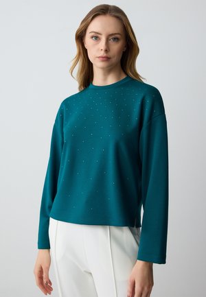 Teal sweatshirt with a round neckline and long sleeves, features scattered small embellishments, relaxed fit, and soft texture.