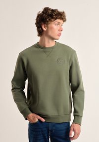 Sudadera verde oliva hecha de una mezcla de algodón, con un cuello redondo, puños acanalados y un pequeño logo en relieve en el pecho.