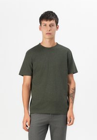 Dunkelgrünes Kurzarm-T-Shirt aus weichem Stoff, mit Rundhalsausschnitt und lässiger Passform. Graue Hosen mit dezenter Textur.