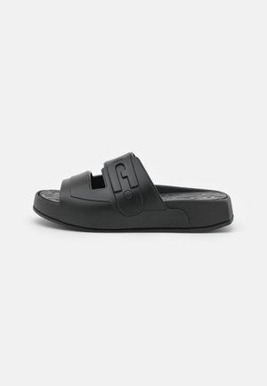 Sandalia de goma negra con diseño de punta abierta, correa ajustable con detalles del logotipo y suela texturizada para un mejor agarre.