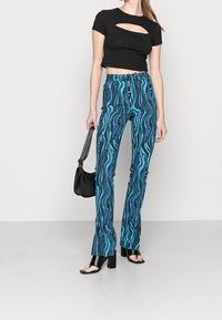 Svart kort topp med utskärning, tillsammans med blå mönstrade utsvängda byxor med virvlande mönster. Modellen håller en svart axelväska.