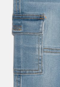 Tissu en denim bleu clair avec des coutures orange contrastantes et un détail de poche cargo, affichant une texture lisse et un design moderne.