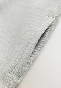 Hellgrauer Stoff mit strukturiertem Oberflächen, gekennzeichnet durch eine gefaltete Kante und eine Nahtdetail, das ein glattes und strapazierfähiges Material präsentiert.