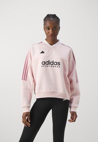 Roze Adidas sweatshirt met een hoge kraag, logo en drie roze strepen langs de mouwen. Gekozen in combinatie met zwarte sportlegging.