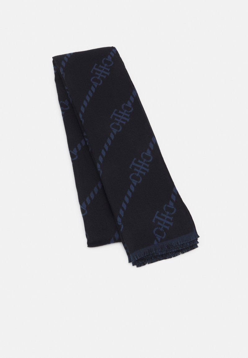 Écharpe bleu foncé avec un motif discret de logo diagonal et des extrémités à franges, soigneusement pliée sur un fond clair uni.