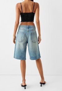 Vaaleansiniset farkkushortsit, joissa on väljä istuvuus, keskipituisuus ja kaksoistakaposkicha. Yhdistettynä mustan lyhyen yläosan ja korkokenkien kanssa.