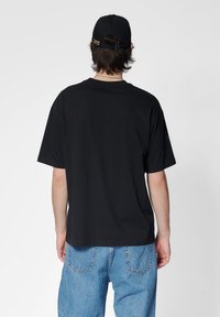 Svart bomulls T-shirt med korta ärmar och avslappnad passform, bärs med ljusblå denimjeans. Enkelt mönster, inga synliga mönster eller logotyper.