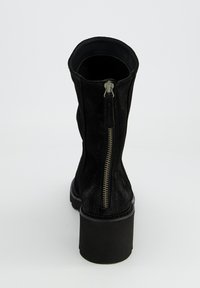 Bottines en daim noir avec un talon épais et un zip sur le côté. Texture lisse et bout rond avec un design simple.