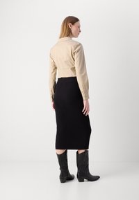 Jacheta bej scurtă cu mâneci lungi, combinată cu o fustă midi neagră cu striații și cizme negre de cowboy cu broderie decorativă.