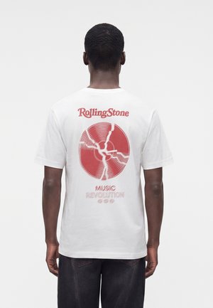 Muž nosiaci biele tričko s červenou grafikou popraskanej vinylovej platne a text "Rolling Stone Music Revolution" na chrbte, otočený chrbtom.