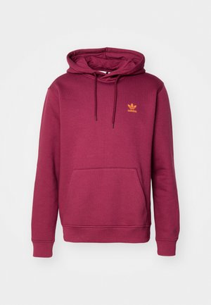 Mörk röd hoodie i mjukt tyg med en framficka, dragsko för huva och en liten orange Adidas-logotyp på bröstet.