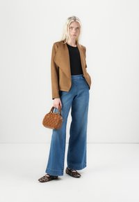 Braun drapierter Blazer über einem schwarzen Top, blaue weite Jeans, braune strukturierte Handtasche und schwarze Ballerinas mit Leopardenmuster.