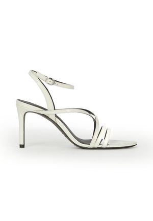 Biała sandałka na wysokim obcasie z cienkim paskiem na kostkę, trzema paskami z przodu i smukłym obcasem typu szpilka na białym tle.