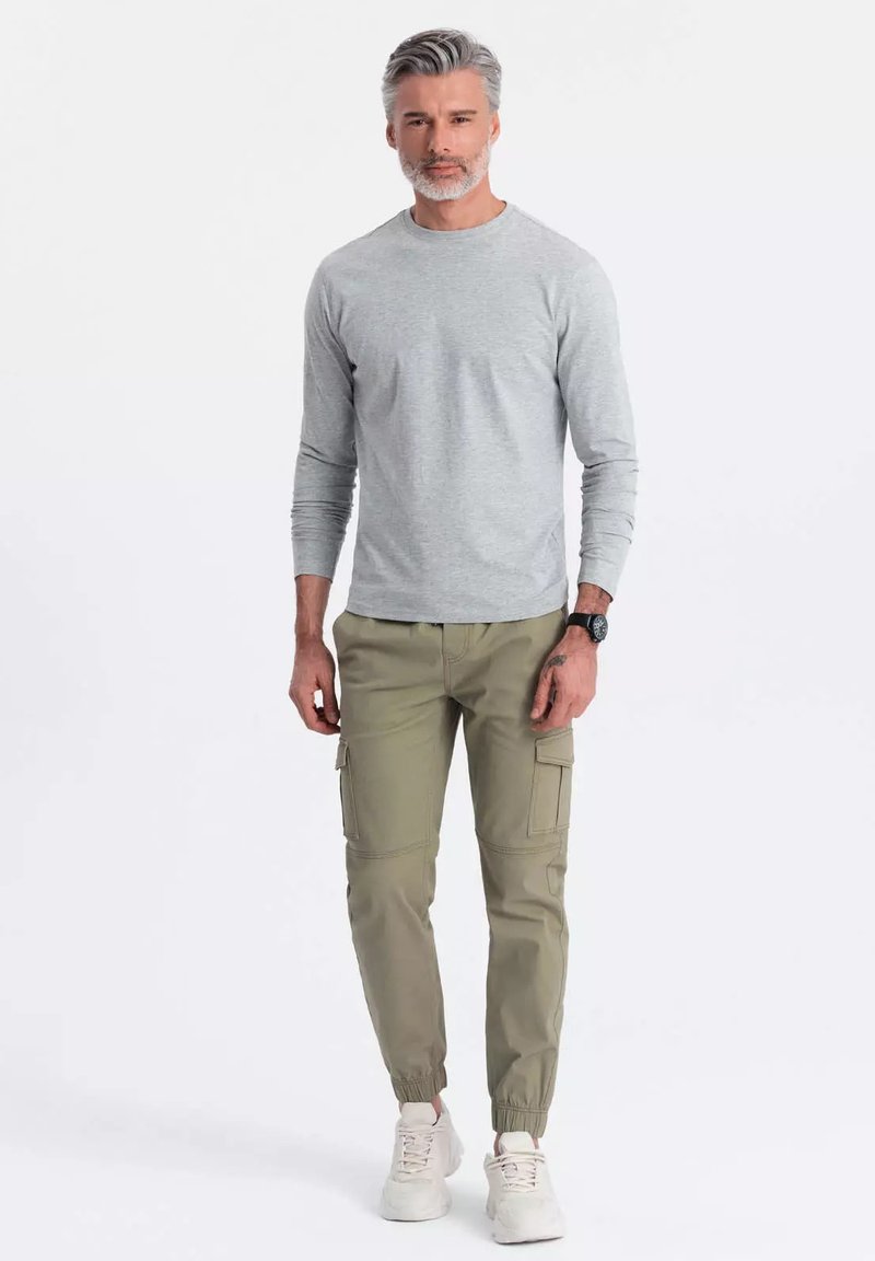 Harmaa pitkähihainen paita yhdistettyinä oliivinvihreisiin cargo-housuihin, joissa on joustavat hihansuut ja useita taskuja, sekä valkoiset lenkkarit.